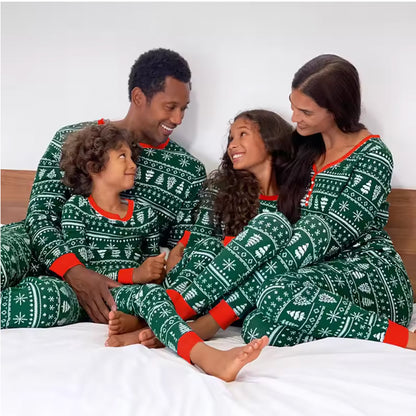 Family of four wearing matching green Christmas pajamas with red accents on a bed.